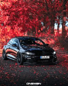 a black car parked on the side of a road in front of trees with red leaves