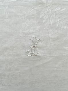 an embroidered monogram on the side of a white linen material with leaves and vines