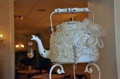 a white teapot with pearls on it hanging from a wall in a restaurant or bar