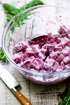 a glass bowl filled with diced food next to a knife