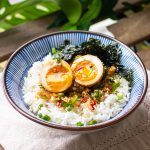 a bowl filled with rice, meat and vegetables on top of a wooden table next to a plant