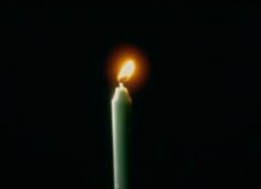 a lit candle in the dark with its light shining on it's side and black background