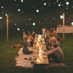 a group of people sitting at a long table with lights strung from the ceiling over them