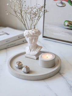 a white marble tray with a candle and some flowers in it on top of a table