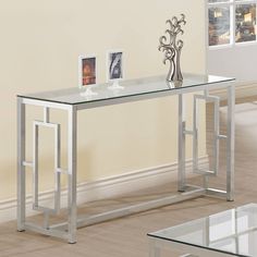 a glass and metal console table with two pictures on the top, in front of a beige wall