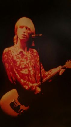 a woman with blonde hair holding a guitar in front of a microphone and singing into a mic