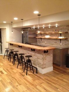 an empty kitchen with bar stools and lights on the ceiling, along with wooden flooring