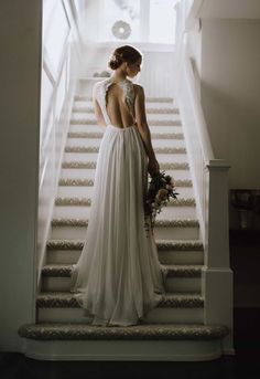 a woman in a wedding dress standing at the bottom of stairs with her back to the camera