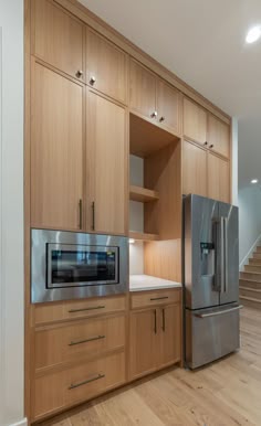 a kitchen with wooden cabinets and stainless steel refrigerator freezer combo in the center, along with stairs leading up to the upper level