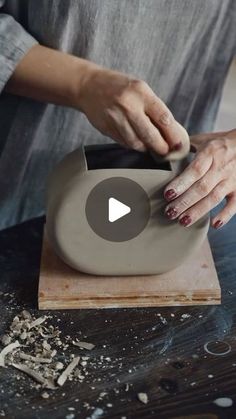 a woman is making a vase out of clay on a wooden block with her hands