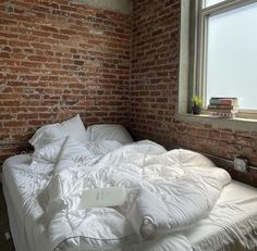 an unmade bed in front of a brick wall with a laptop computer on it