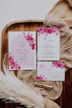 the wedding stationery is laid out on a wooden tray, with pink flowers and greenery