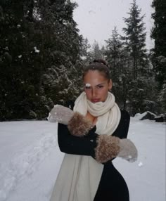 a woman is standing in the snow with her arms crossed and wearing mittens on