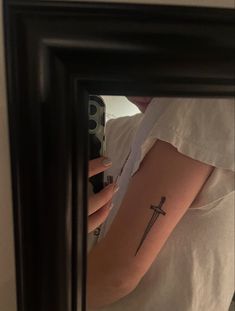 a woman with a cross tattoo on her arm is looking in a mirror and holding a cell phone