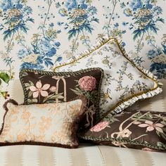 four pillows on a couch with floral wallpaper in the back ground and behind them is a bouquet of flowers