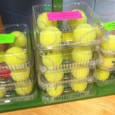 tennis balls are stacked in plastic containers on the shelf next to each other, with pink tags attached to them