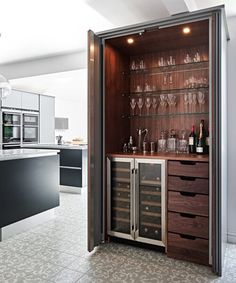 an open cabinet with wine glasses and bottles in it on the floor next to a counter