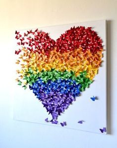 a heart made out of colored butterflies on a white wall with the colors of rainbow