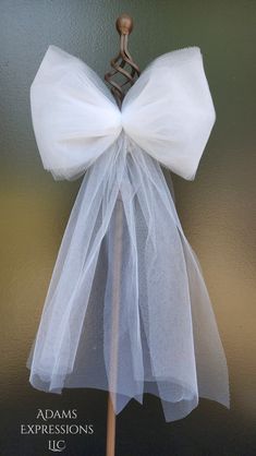 a white tulle bow on top of a wooden stick in front of a wall