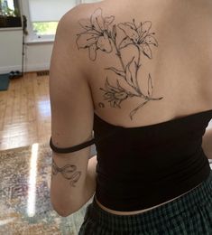 the back of a woman's shoulder with flowers on her left arm and tattoos on her right arm