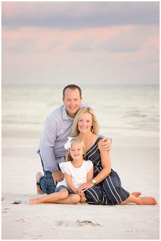 a man, woman and child are sitting in the sand at the beach with their arms around each other