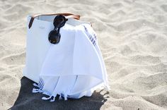 a white bag sitting on top of a sandy beach next to a pair of sunglasses