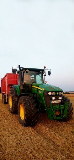 a green tractor is parked in the middle of a field with a red trailer behind it