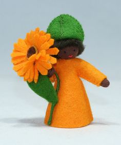 an orange doll with a green hat holding a yellow flower