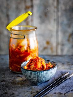 a bowl full of food next to a jar filled with sauce and chopsticks