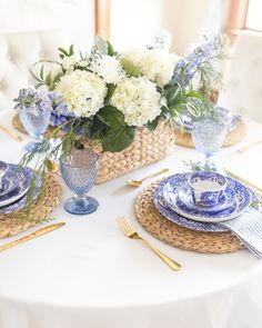 a table set with blue and white plates, silverware and flowers in a wicker basket