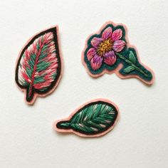 three embroidered patches with pink flowers and green leaves on white paper, one has a single flower in the middle