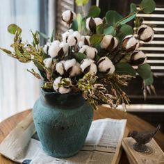 a green vase filled with cotton sitting on top of a table next to a book