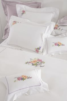 a white bed topped with lots of pillows next to a pillow case filled with pink and yellow flowers