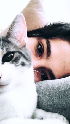 a woman laying down next to a gray and white cat