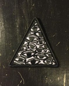 a triangle patch with an eye design on the front and back, sitting on top of a metal surface