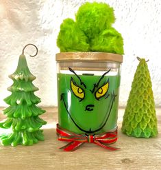 a green candle with yellow eyes surrounded by small christmas trees and other holiday decorations on a wooden table