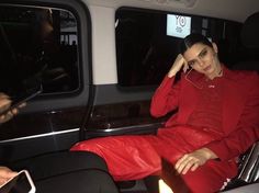 a woman sitting in the back of a car talking on a cell phone while wearing a red outfit