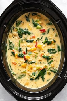 a black crock pot filled with soup and vegetables on top of a white table