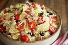 a bowl filled with pasta and vegetables on top of a wooden table next to a striped napkin