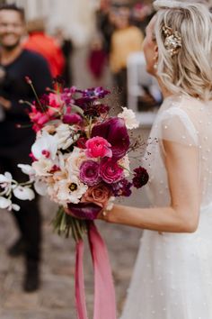 a woman holding a bouquet of flowers in her hand while standing next to another person