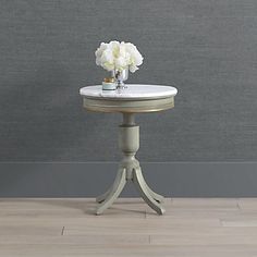 a small table with flowers on it in front of a gray wall and wooden floor