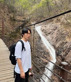 a young man standing on a bridge next to a waterfall