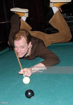 a man in brown shirt playing pool with two legs up on the billiard table