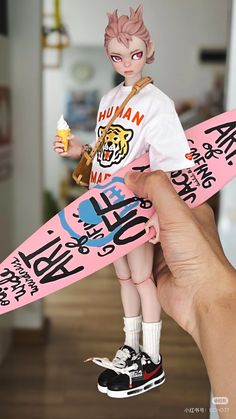 a hand holding a small doll with a pink skateboard