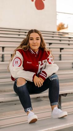 a young woman sitting on the bleachers wearing a red and white varsity jacket