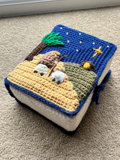 a crocheted book with sheep and palm trees on it sitting on the floor