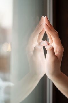 a person is holding their hands up to the side of a glass window with light coming through it