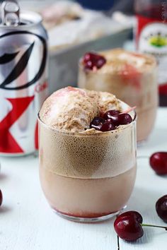 two glasses filled with ice cream and cherries on top of a table next to cans of soda