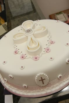 a white cake with pink flowers and a cross on the top is sitting on a table