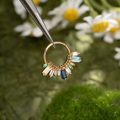 a pair of gold hoop earrings with multicolored stones hanging from a hook on a green mossy surface